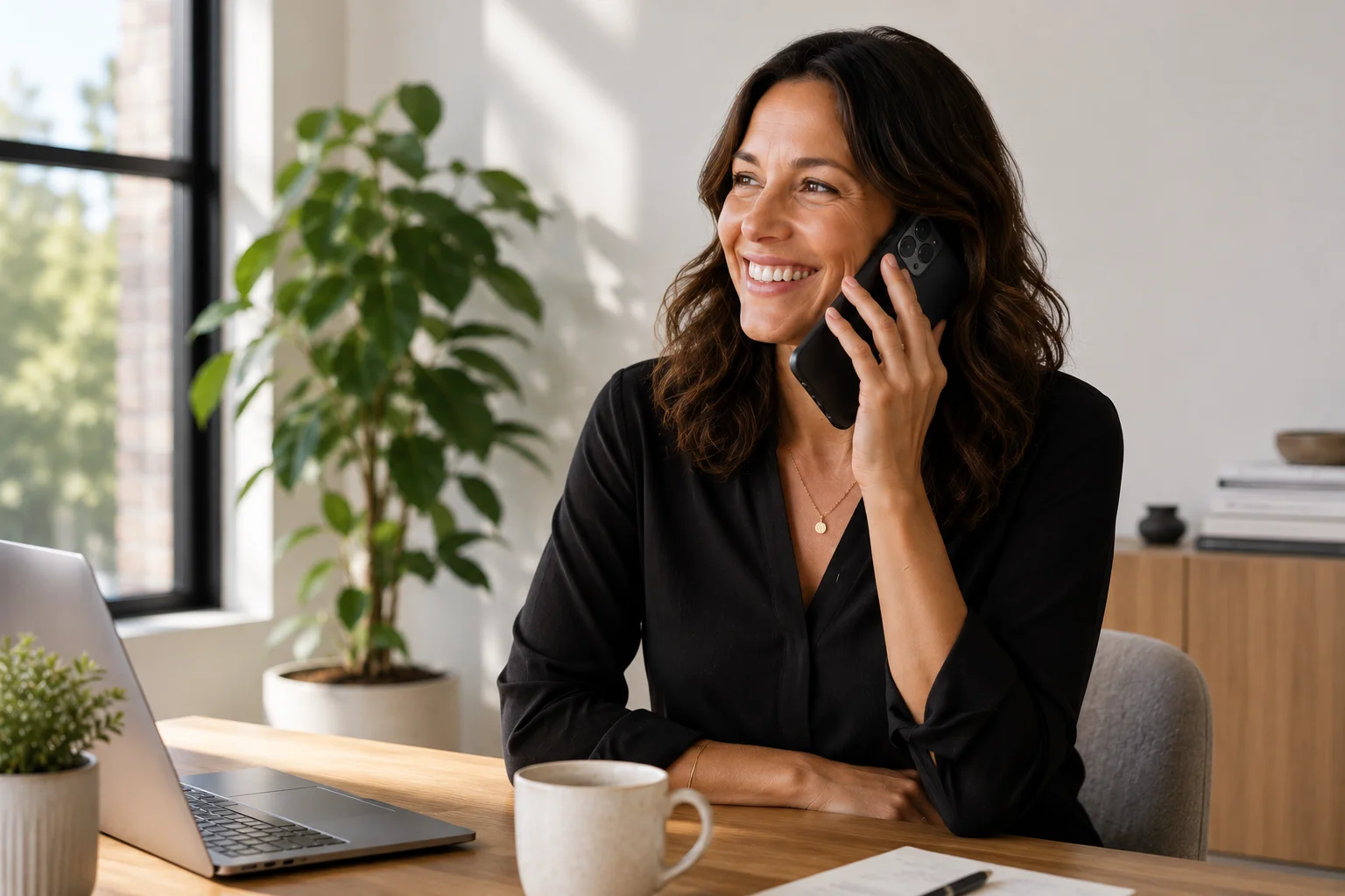 Professionnelle souriante au téléphone à son bureau avec un ordinateur portable
